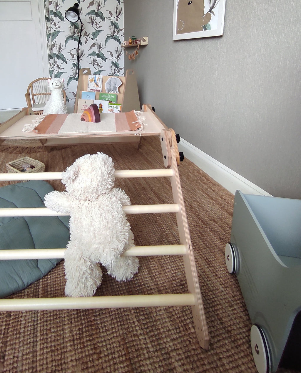 8. Montessori climbing set with a plush bear climbing the rungs, in a playroom with a toy cart and decorative wallpaper.