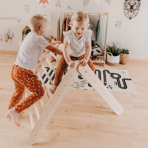 2. Two children playing on Montessori Climbing Triangle in a playroom with wooden floor and wall decorations