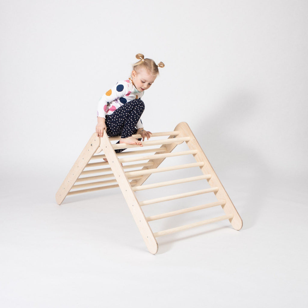 1. Young girl climbing on Montessori Climbing Triangle in a studio setting, wearing a colorful polka dot top and black pants