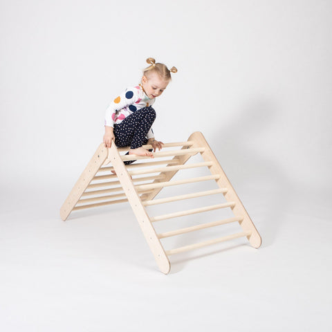1. Young girl climbing on Montessori Climbing Triangle in a studio setting, wearing a colorful polka dot top and black pants