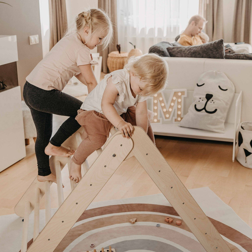 8. Two children climbing on Montessori Climbing Triangle in a living room setting with toys and cushions