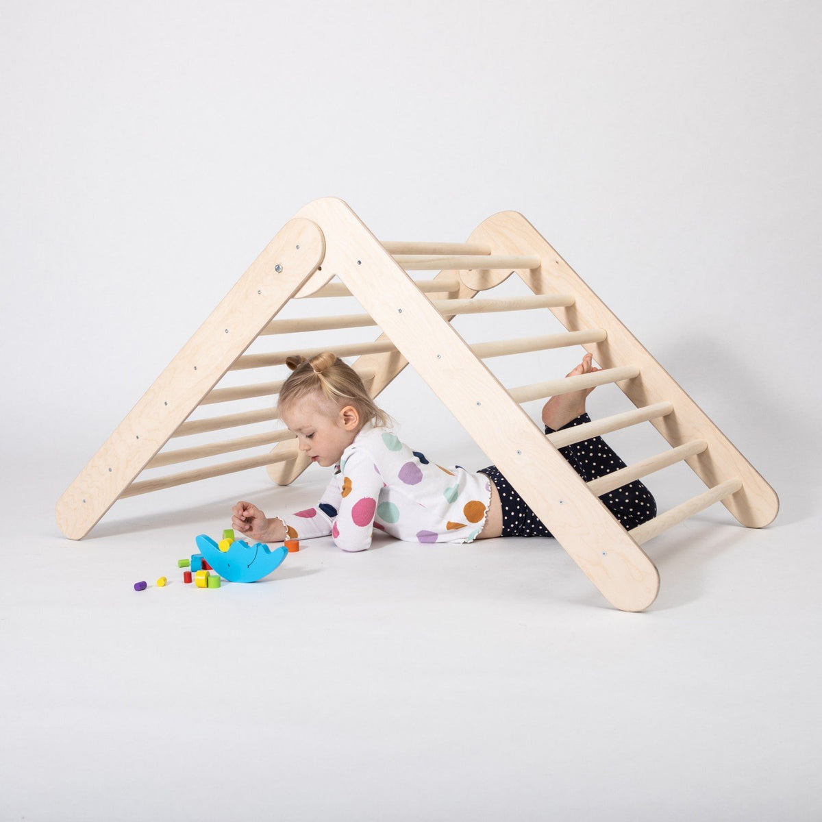 6. Young girl playing under Montessori Climbing Triangle in studio setting, wearing a colorful polka dot top