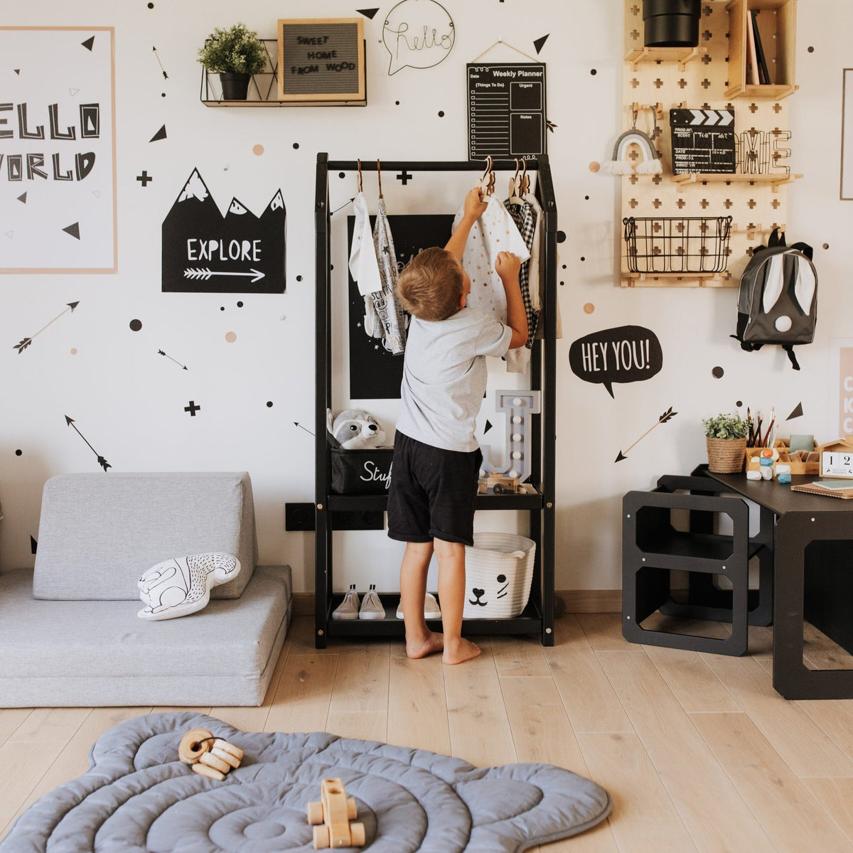 1. Child reaching for clothes on a black house-shaped clothing rack in a decorated kids' room