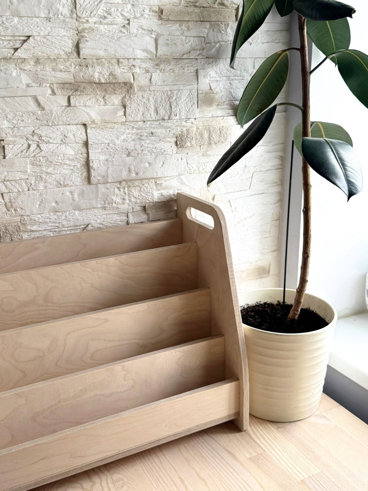 1. Montessori wooden book display in a modern room setting with a potted plant, highlighting its natural finish and minimalist style.