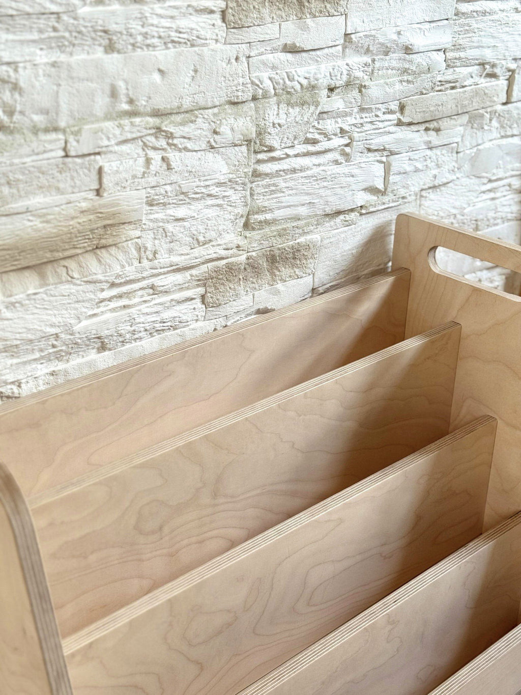 3. Close-up of the Montessori book display's birch plywood texture and tiered design against a stone wall background.