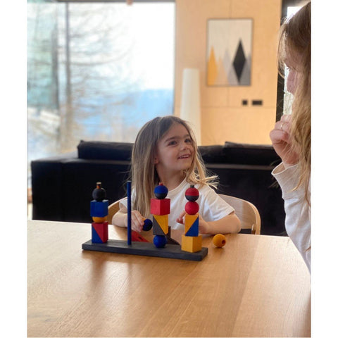 1. Child playing with Montessori-inspired stacking toy with colorful geometric shapes at a wooden table