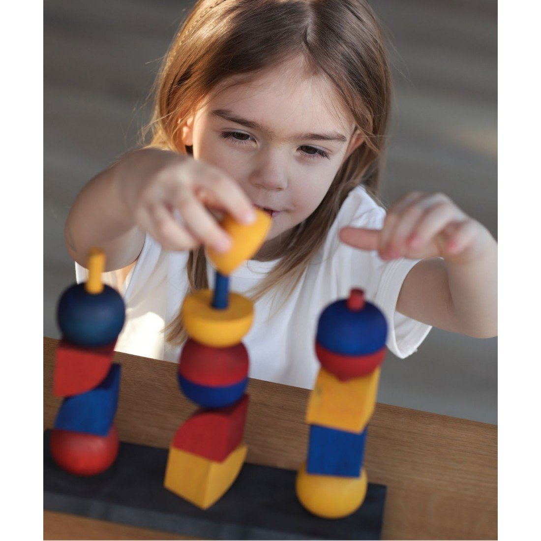 1. Young girl playing with colorful wooden stacking toy on a table, natural light