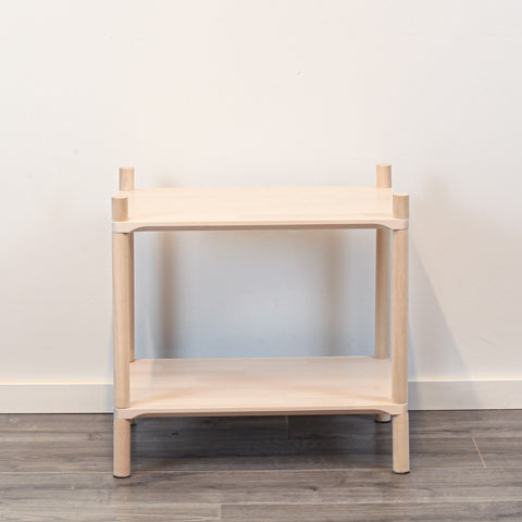 2. Studio shot of Montessori-inspired wooden shelving unit with two shelves, made from natural birch wood, against a plain white wall and wooden floor.