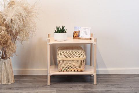 1. Montessori-inspired wooden shelving unit with two shelves, featuring a potted plant and a calendar on top, next to a vase with dried flowers, set against a white wall and wooden floor.