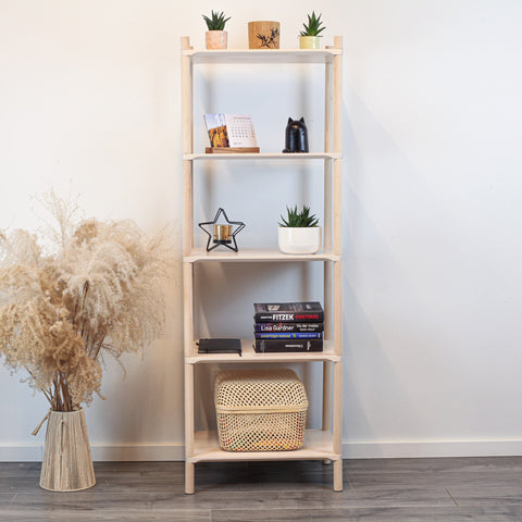 1. Montessori-inspired wooden shelving unit with five shelves, decorated with books, plants, and ornaments, placed against a white wall with a vase of pampas grass on the side