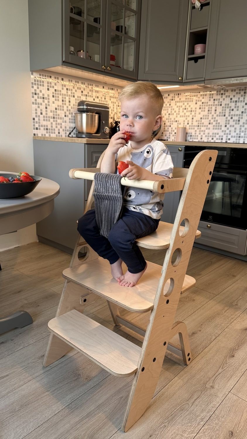 1. Child sitting on wooden Montessori learning tower in a kitchen setting