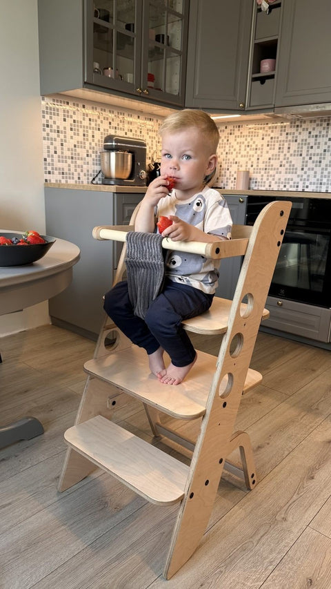 1. Child sitting on wooden Montessori learning tower in a kitchen setting