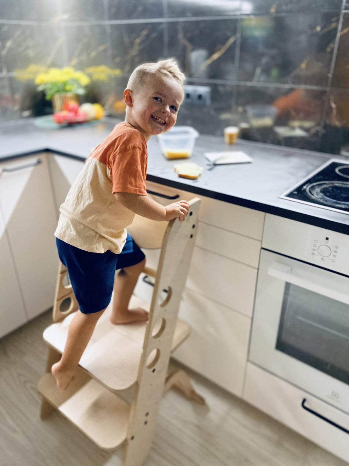 1. Child standing on wooden Montessori learning tower at kitchen counter