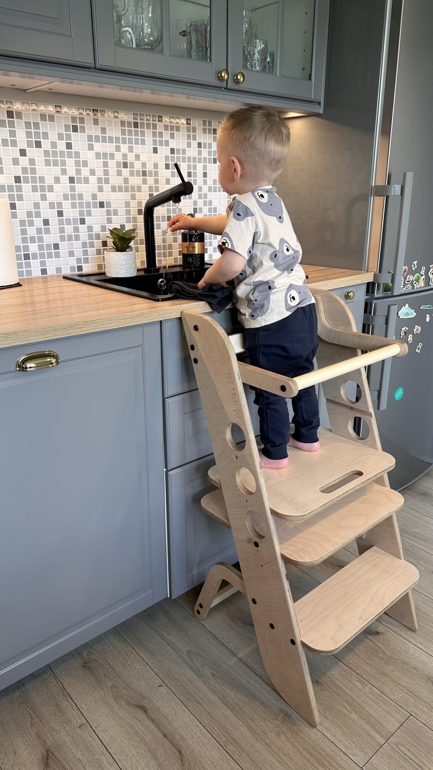 1. Toddler using wooden Montessori learning tower at kitchen sink