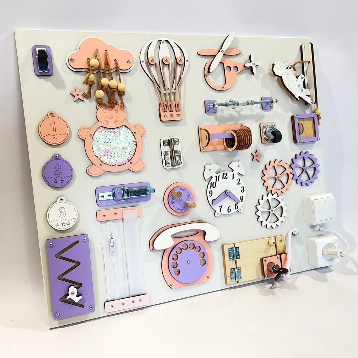 2. Montessori busy board with purple and orange elements on white background, showcasing interactive features like gears and switches.