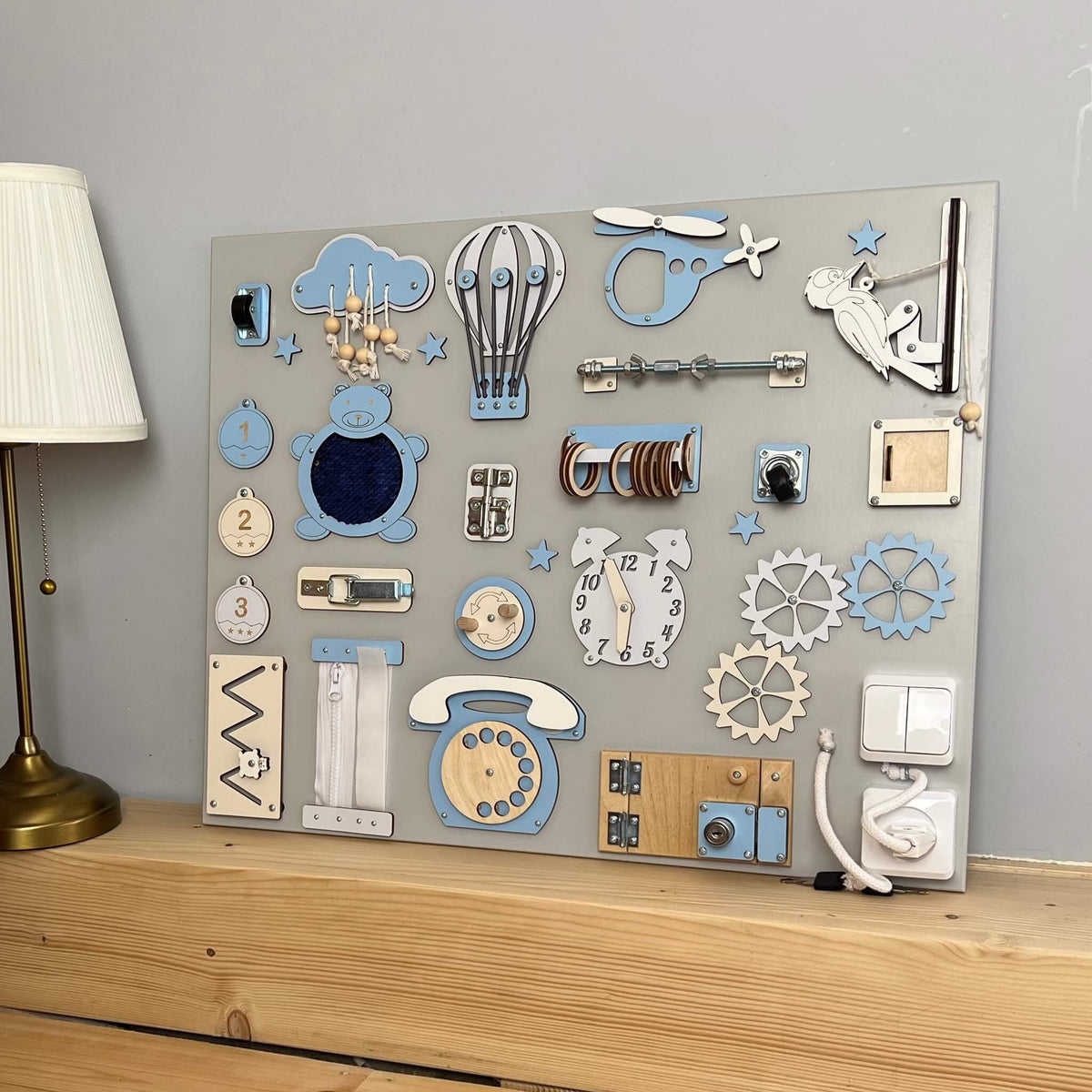 2. Montessori busy board with blue and white elements on a wooden shelf, featuring interactive components like gears and switches.