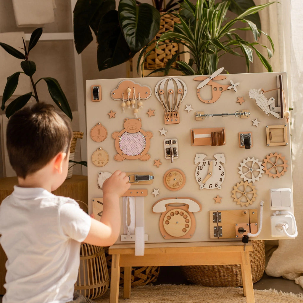 1. Child interacting with Montessori busy board featuring beige and orange elements, set on an easel in a cozy room with plants.