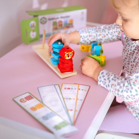 5. Child stacking blue and red animal blocks on Montessori puzzle pyramid with pattern cards on pink table