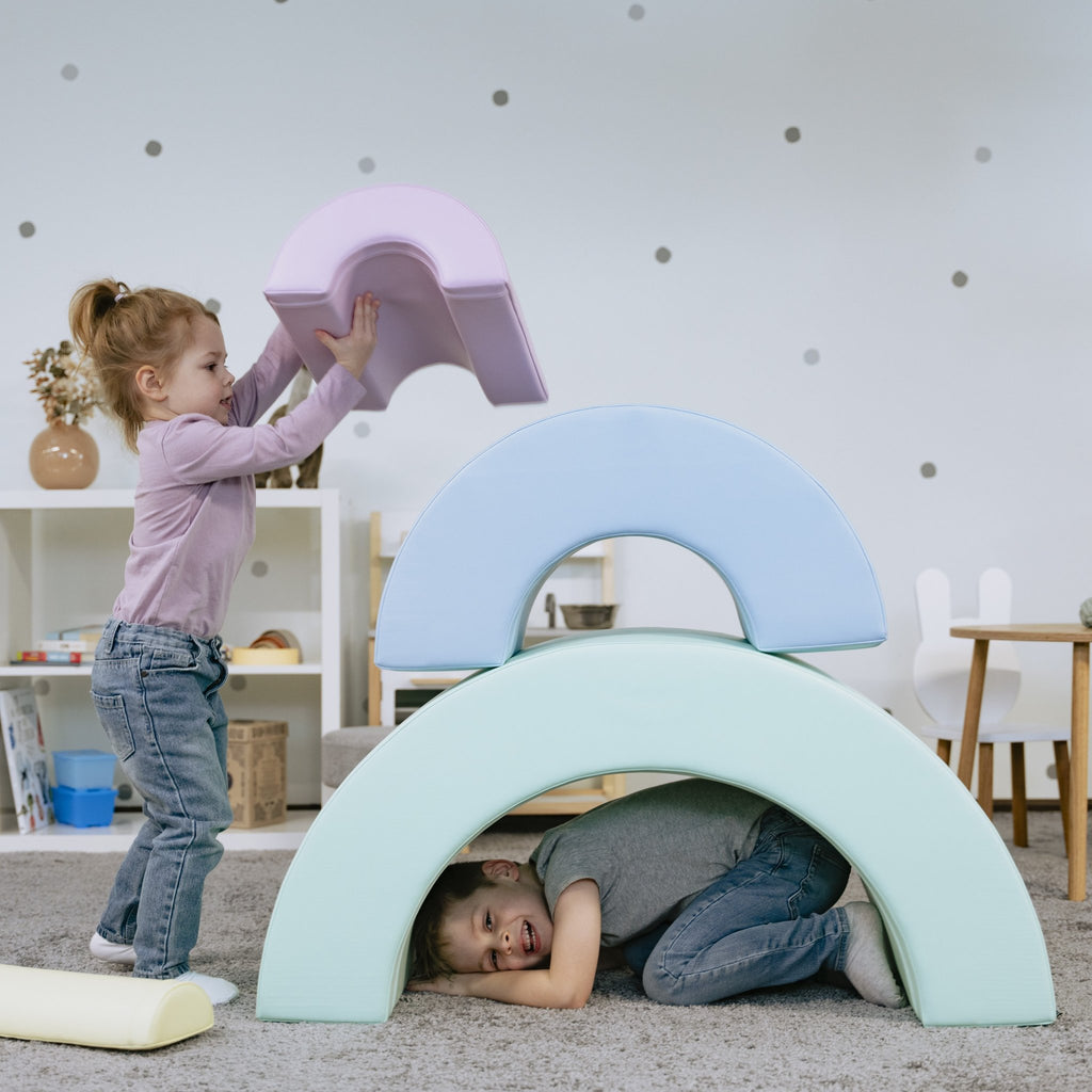 11. Girl stacking pastel rainbow soft play pieces with boy underneath in playroom
