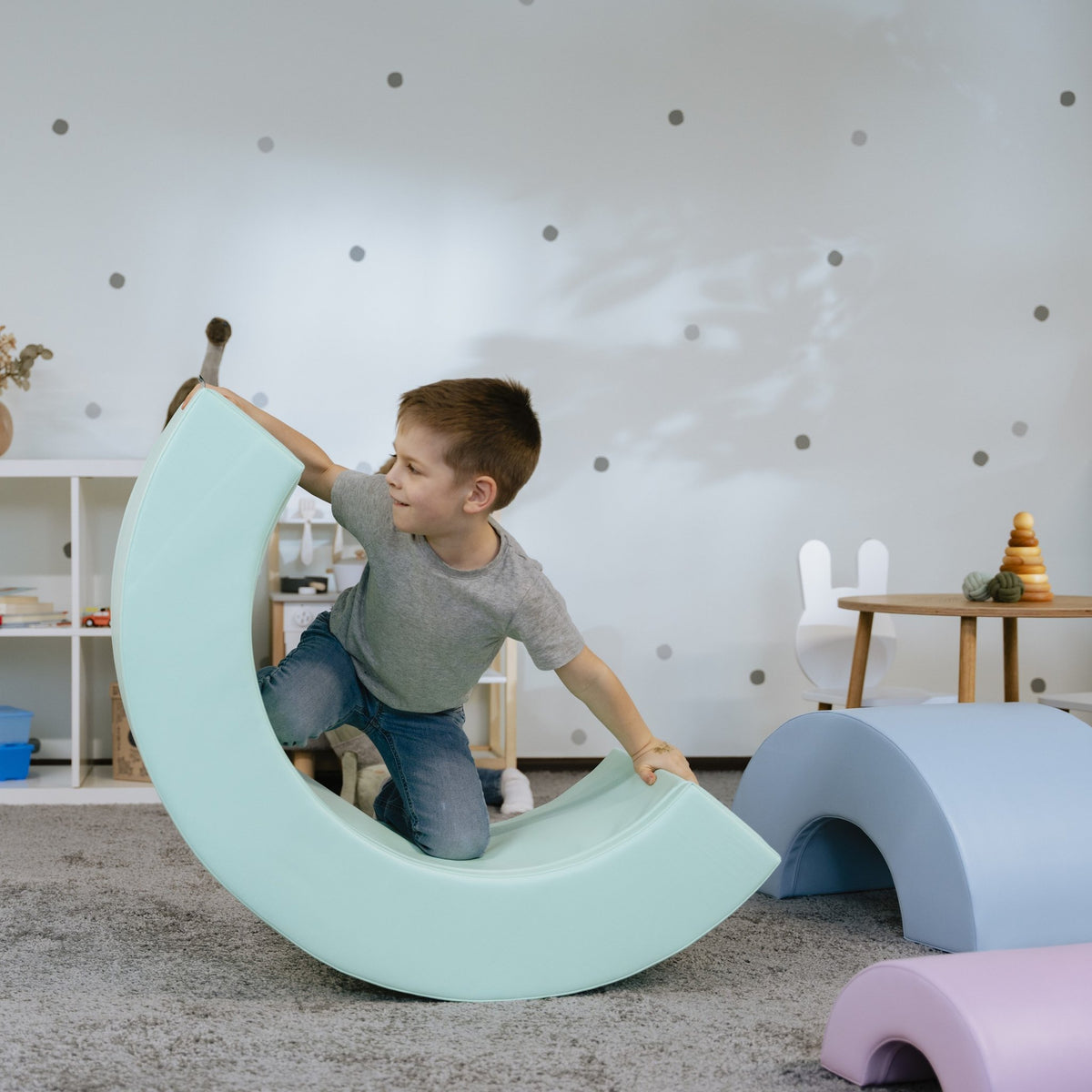 7. Boy lifting pastel rainbow soft play piece in playroom