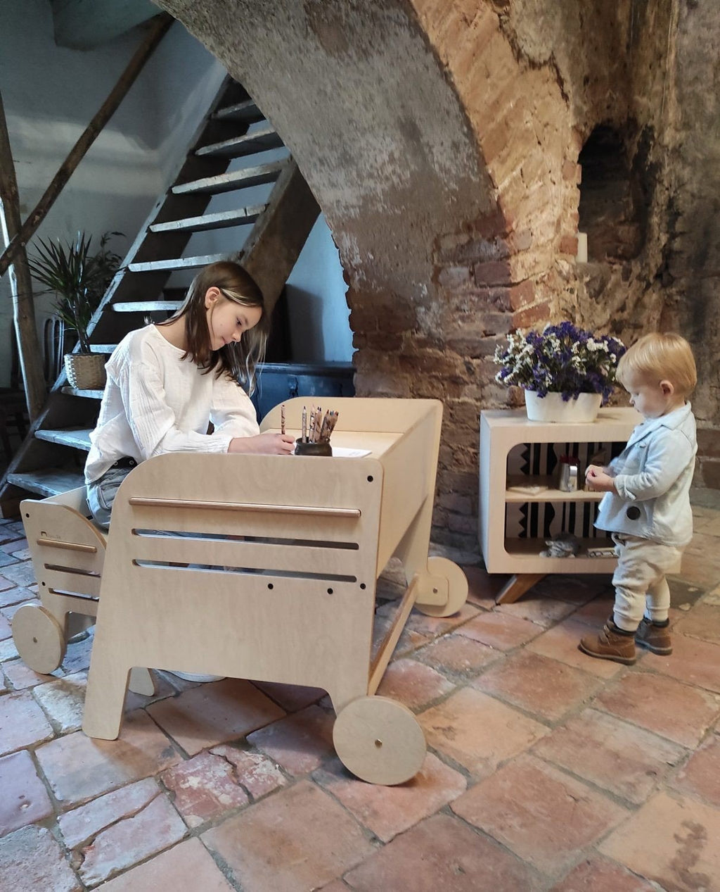 1. Woman and child using Luula Montessori table and chair set in rustic interior, highlighting adjustable design and personal space for creativity