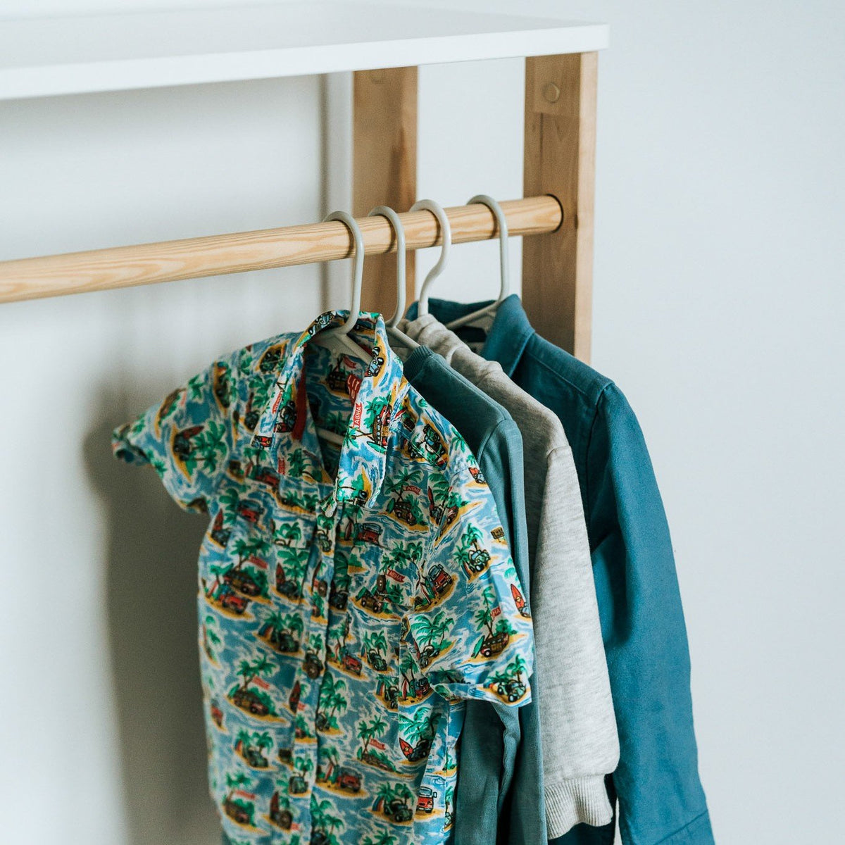 3. Close-up of children's shirts hanging on a natural wood clothes rail in a Montessori wardrobe, highlighting fabric patterns and colors