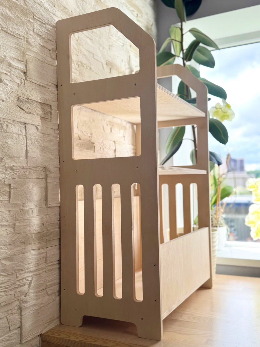 1. Montessori wooden shelf in natural birch plywood placed in a room with plants and stone wall background