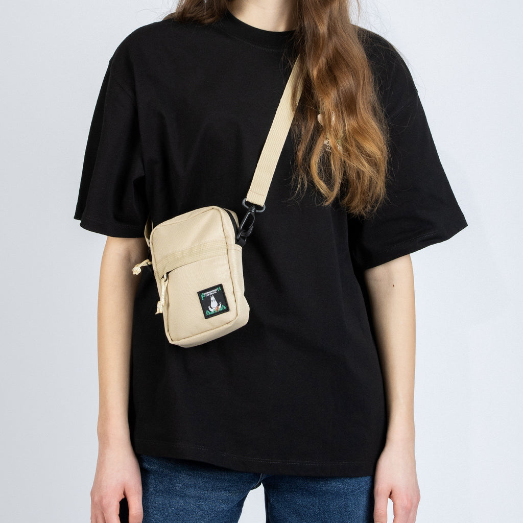 1. Woman wearing beige Moomin 80 cross body bag by NordicBuddies over black t-shirt and jeans
