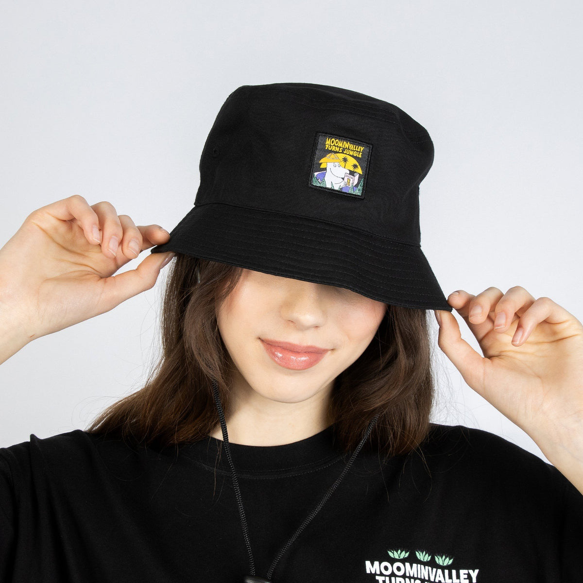1. Woman wearing Moomin Jungle black bucket hat by NordicBuddies, showcasing playful Moomin theme