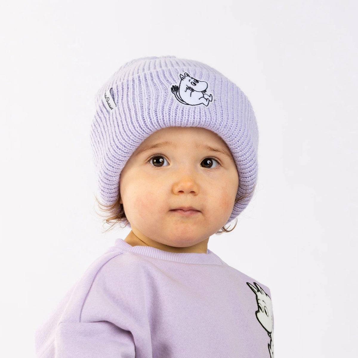 1. Child wearing lavender Moomintroll beanie with felt patch, smiling in studio setting