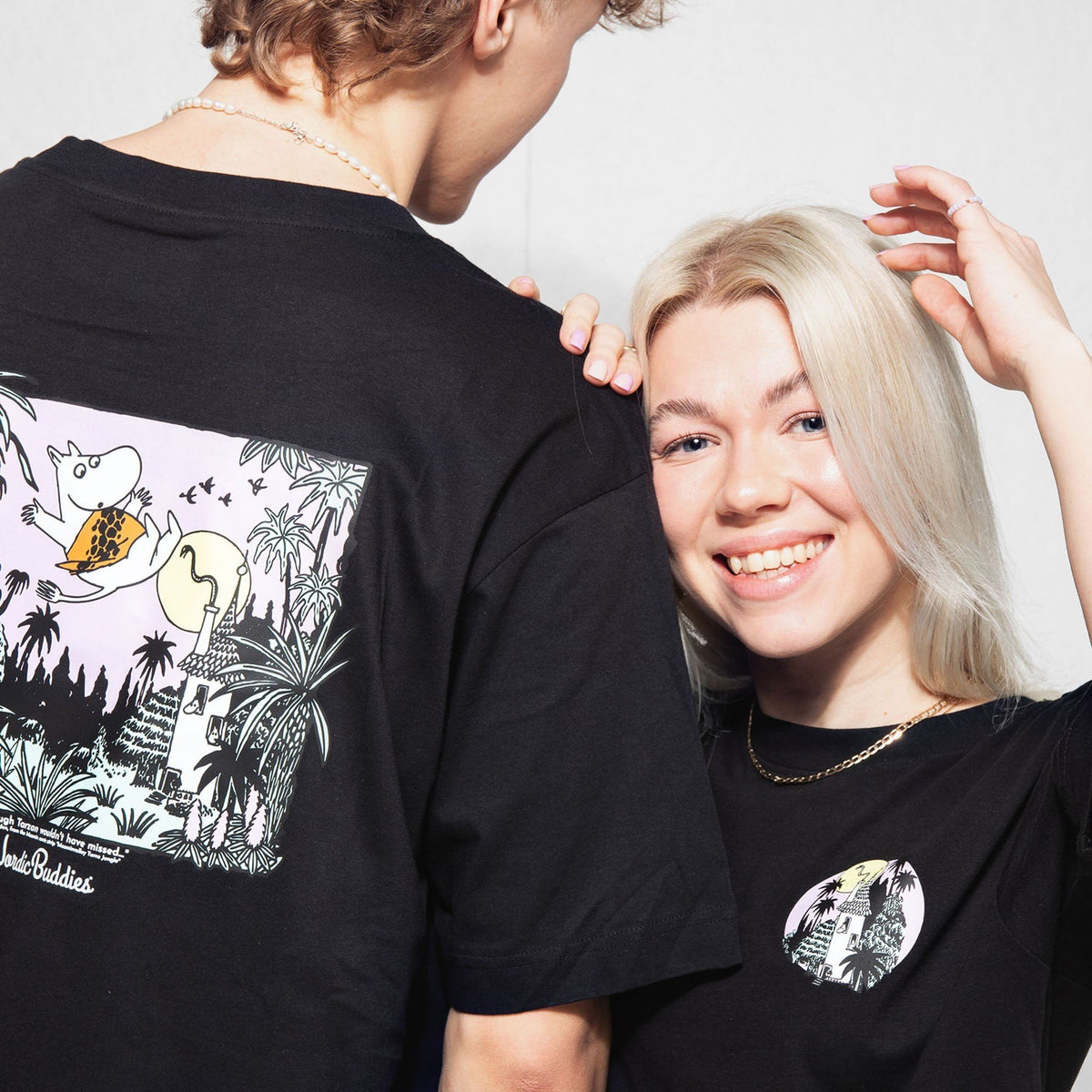1. Two people wearing black Moomin unisex t-shirts with jungle design, one showing back print and the other front logo, smiling in a casual setting
