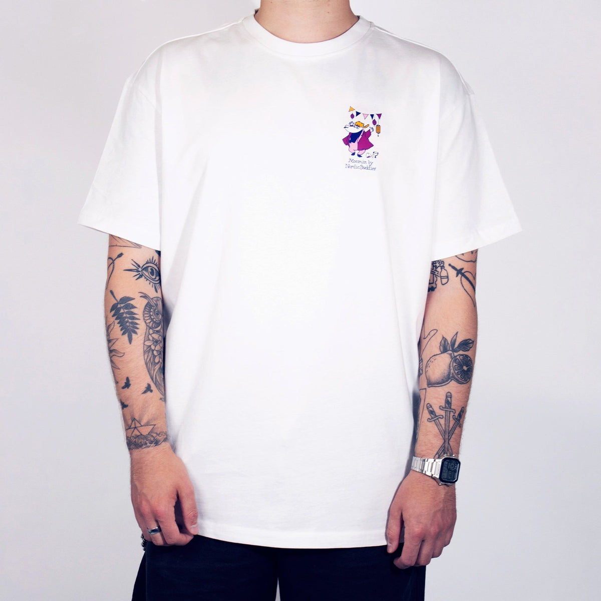 2. Person wearing white unisex Moomin Party T-shirt with small front print, arms by sides, studio background