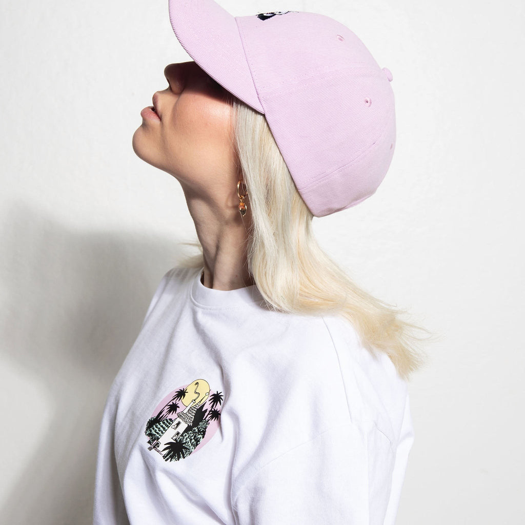 6. Woman wearing white Moomintroll Jungle t-shirt with small front graphic, pink cap, side profile