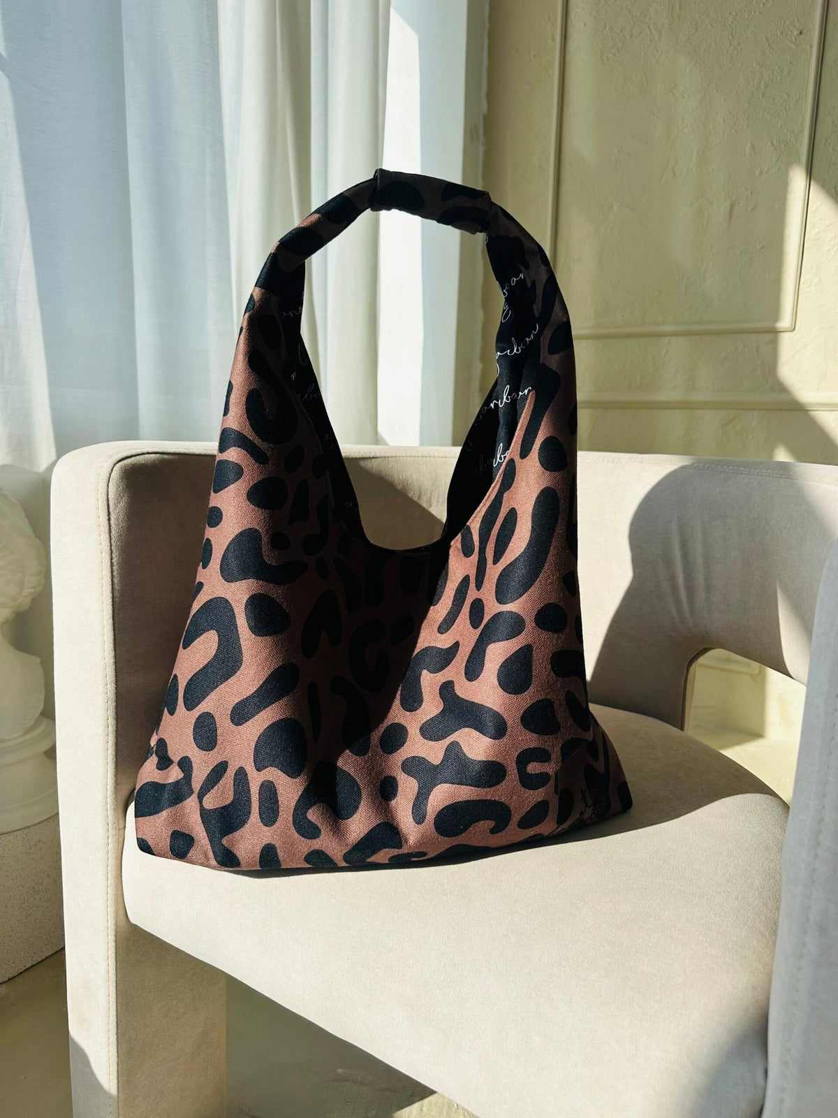 5. Garbanota Moon Bag in classic leopard print, placed on a beige chair in natural light