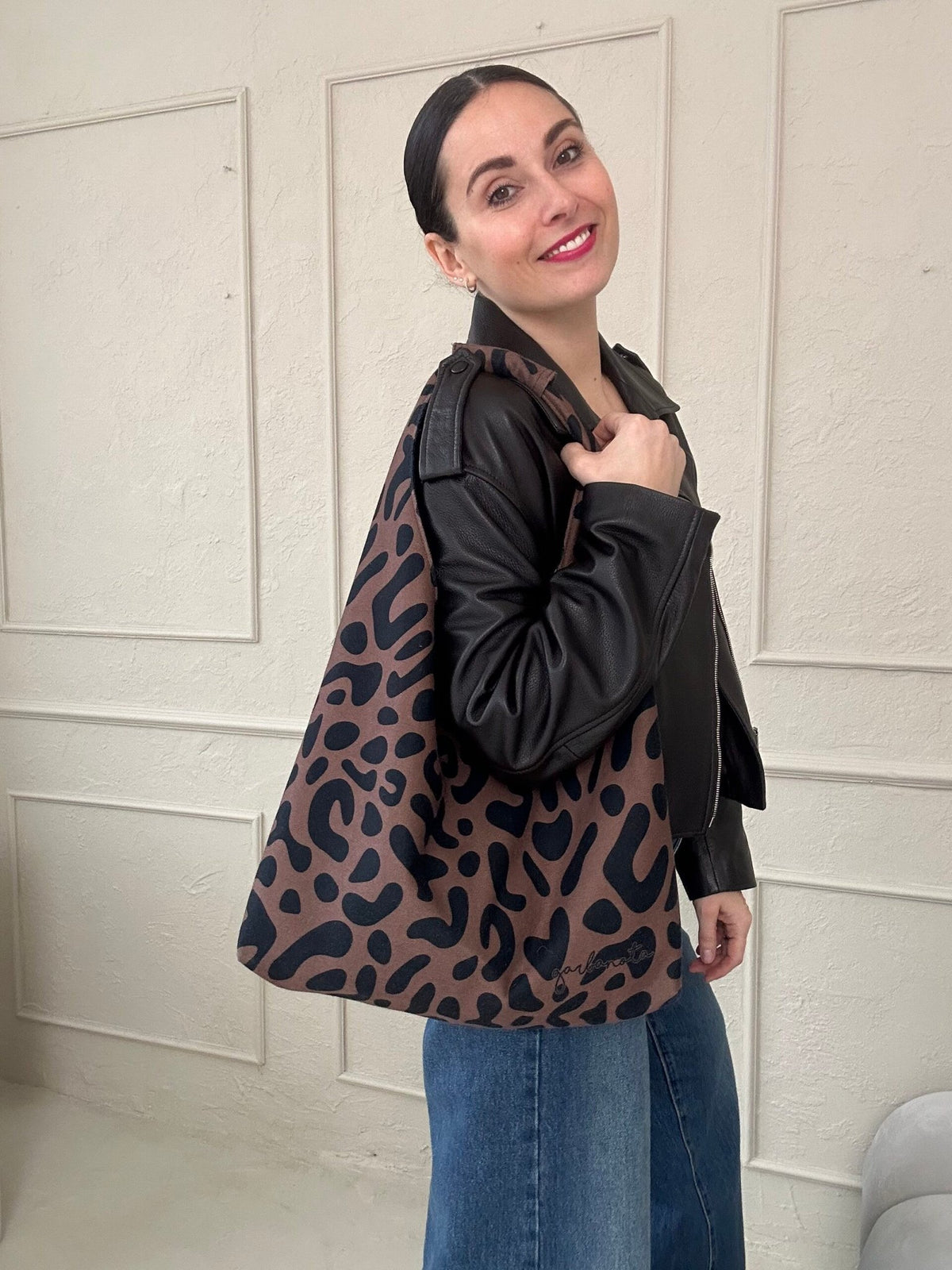 1. Woman holding Garbanota Moon Bag in classic leopard print, styled with black leather jacket and jeans