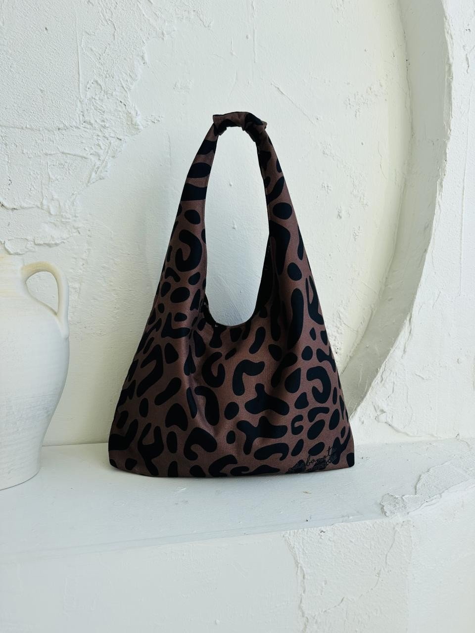 13. Garbanota Moon Bag in classic leopard print, displayed on a white shelf with decorative vase