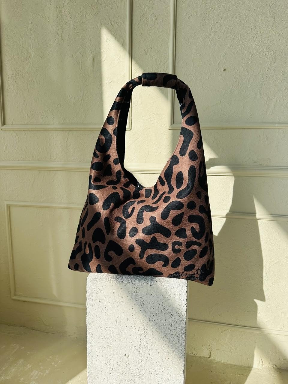 9. Garbanota Moon Bag in classic leopard print, displayed on a white block in a sunlit room
