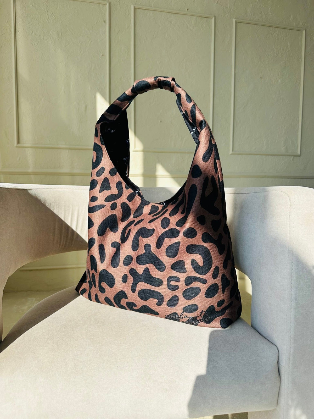 6. Garbanota Moon Bag in classic leopard print, resting on a wooden chair with woven back