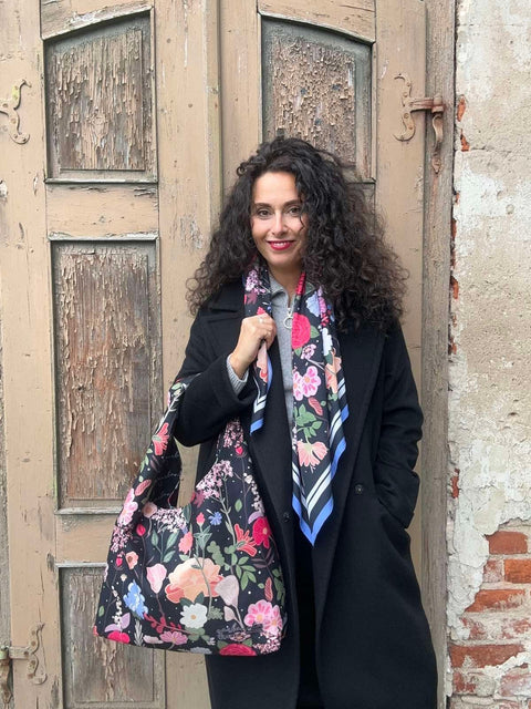 1. Woman holding Garbanota Moon Bag - Curly Summer Night with floral pattern, standing against rustic door