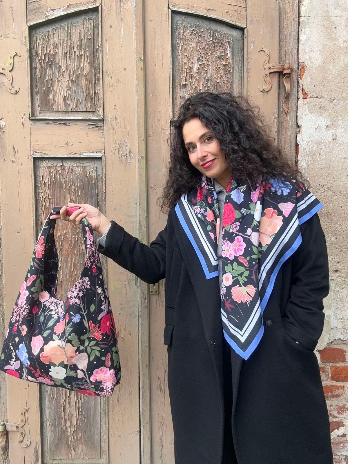 2. Woman displaying Garbanota Moon Bag - Curly Summer Night with floral design, wearing black coat