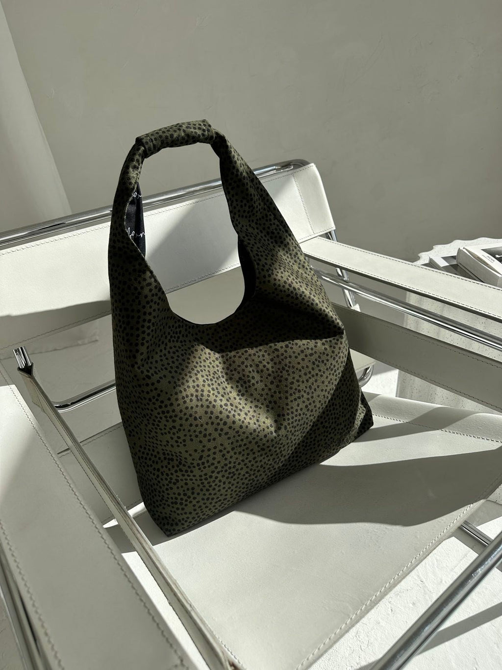 3. Garbanota Moon Bag Heart in khaki polka dots on a white chair, emphasizing its lightweight canvas-like material and chic appearance
