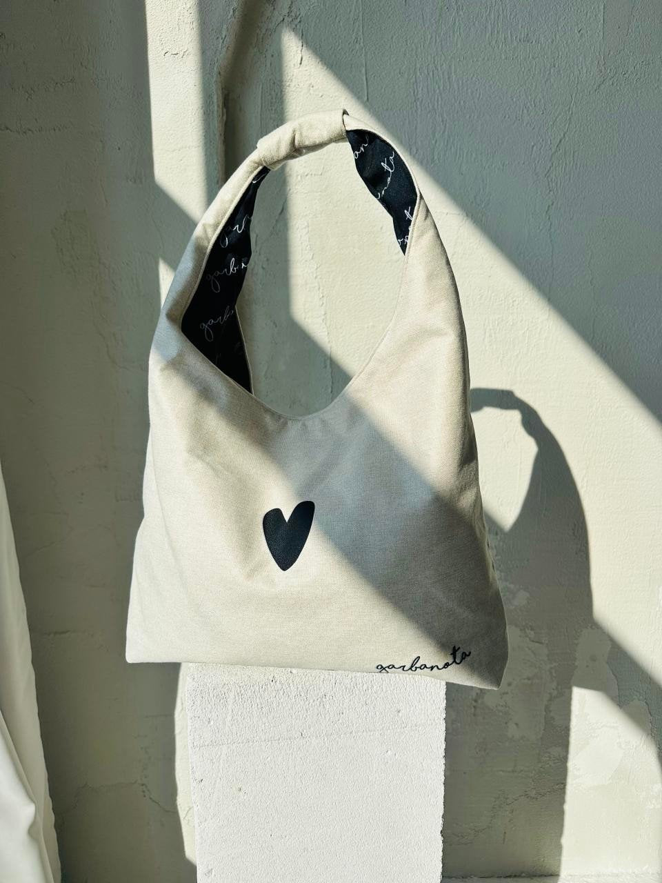 4. Garbanota Moon Bag Heart in white hanging against a textured wall, featuring heart design
