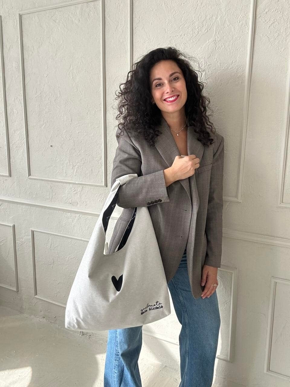 1. Woman holding Garbanota Moon Bag Heart in white, styled with a blazer and jeans