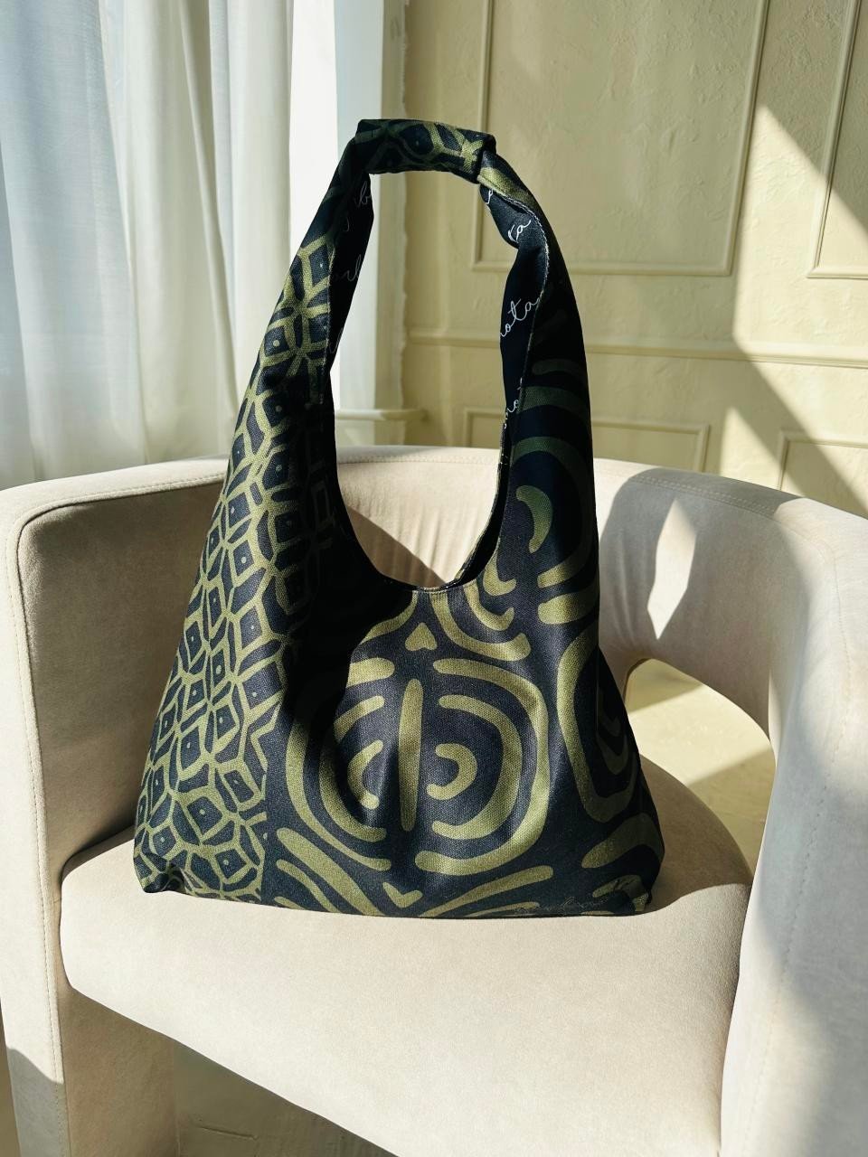 6. Garbanota Moon Bag in khaki pattern on a beige chair, showing elegant design