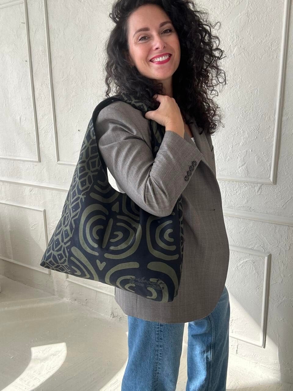 1. Woman carrying Garbanota Moon Bag in khaki pattern, styled with a blazer and jeans, showcasing versatility