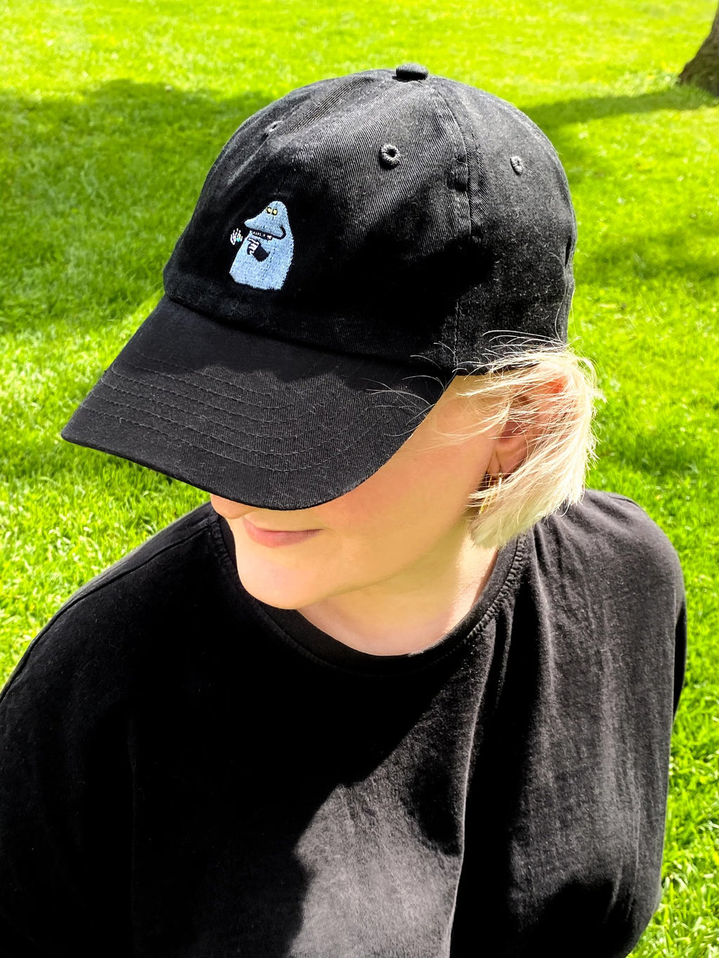 1. Woman wearing The Groke Adult Cap in black by Moomin, styled in a sunny outdoor setting