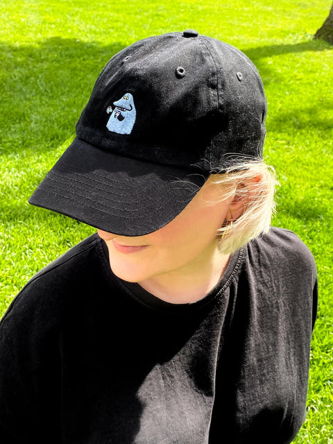 1. Woman wearing The Groke Adult Cap in black by Moomin, styled in a sunny outdoor setting