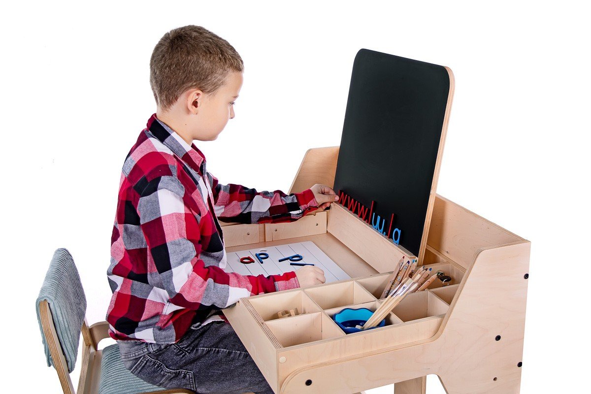 9. Boy using Luula table with chalkboard and storage compartments, highlighting educational play