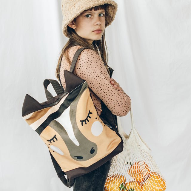 2. Girl wearing Muni horse backpack, holding a net bag with oranges, in lifestyle setting