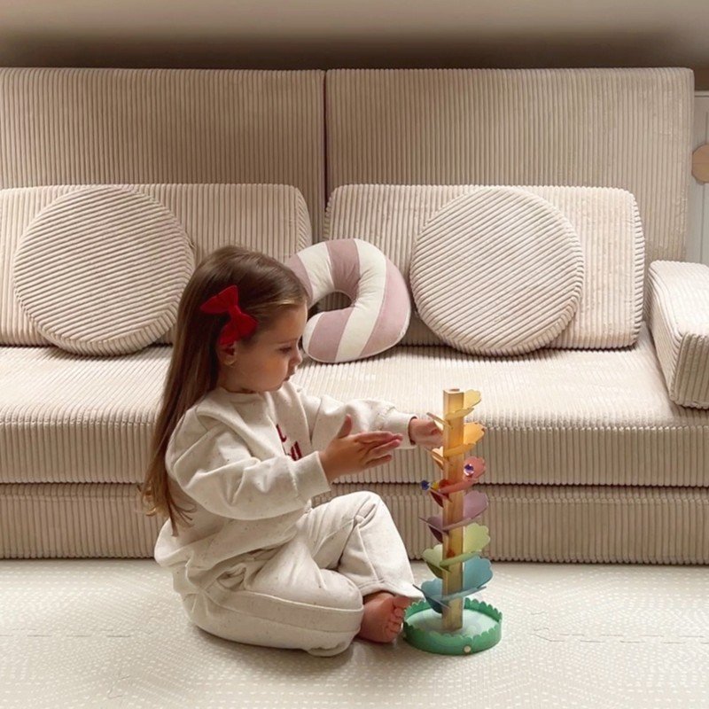 1. Young girl playing with Woopie Let's Go Green musical rainbow wooden ball track on a beige sofa